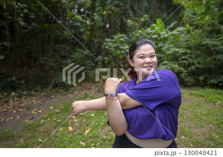Indonesian southeast asian overweight woman in a sporty outfit practices exercise in a public park outdoors. Concept of a Healthy active lifestyle and body inclusivity Indonesian southeast asian overweight woman in a sporty outfit practices exercise in a public park outdoors. Concept of a Healthy active lifestyle and body inclusivity 130048421