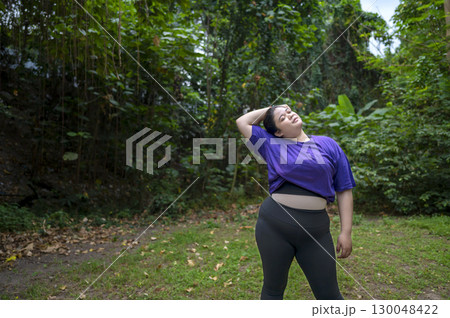 Indonesian southeast asian overweight woman in a sporty outfit practices exercise in a public park outdoors. Concept of a Healthy active lifestyle and body inclusivity Indonesian southeast asian overweight woman in a sporty outfit practices exercise in a public park outdoors. Concept of a Healthy active lifestyle and body inclusivity 130048422