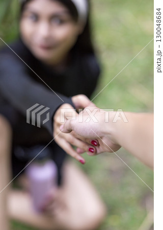 Human hand grabs an Indonesian southeast asian woman in a sporty outfit drinking water after a practice running exercise in a public park outdoors. Concept of a Healthy active lifestyle Human hand grabs an Indonesian southeast asian woman in a sporty outfit drinking water after a practice running exercise in a public park outdoors. Concept of a Healthy active lifestyle 130048684