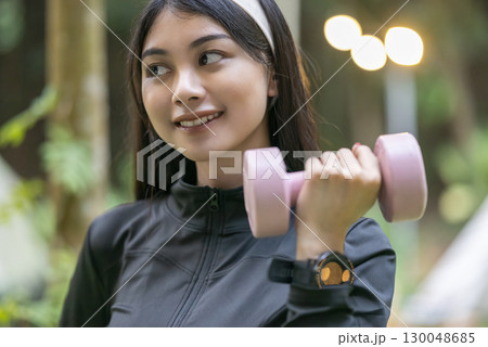 Indonesian southeast asian woman in a sporty outfit practices with a dumbbell in a public park outdoors. Concept of a Healthy active lifestyle 130048685