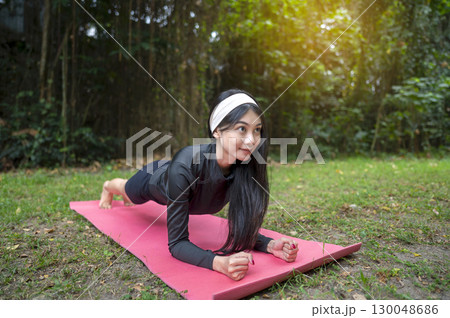 Indonesian southeast asian woman in a sporty outfit practices exercise on a mat in a public park outdoors. Concept of a Healthy active lifestyle Indonesian southeast asian woman in a sporty outfit practices exercise on a mat in a public park outdoors. Concept of a Healthy active lifestyle 130048686