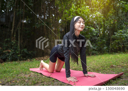 Indonesian southeast asian woman in a sporty outfit practices exercise on a mat in a public park outdoors. Concept of a Healthy active lifestyle Indonesian southeast asian woman in a sporty outfit practices exercise on a mat in a public park outdoors. Concept of a Healthy active lifestyle 130048690