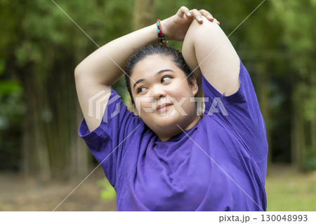 Indonesian southeast asian overweight woman in a sporty outfit practices exercise in a public park outdoors. Concept of a Healthy active lifestyle and body inclusivity Indonesian southeast asian overweight woman in a sporty outfit practices exercise in a public park outdoors. Concept of a Healthy active lifestyle and body inclusivity 130048993