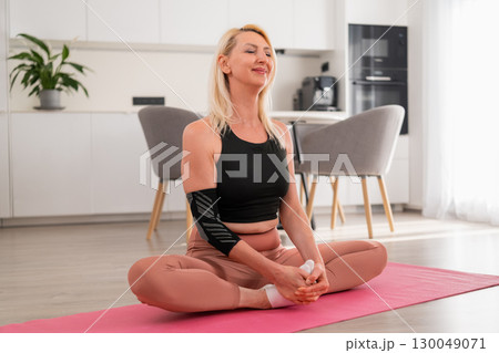 Relaxed blonde woman with close eyes in lotus pose meditating and practicing yoga in contemporary kitchen of modern apartment 130049071