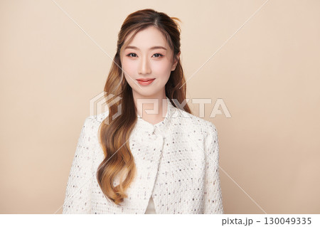 A beautiful young Asian woman with clean, fresh skin against a beige background. Skincare, facial treatment, cosmetology, beauty, and spa. An elegant portrait of an Asian woman. 130049335