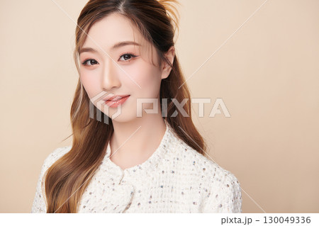 A beautiful young Asian woman with clean, fresh skin against a beige background. Skincare, facial treatment, cosmetology, beauty, and spa. An elegant portrait of an Asian woman. 130049336