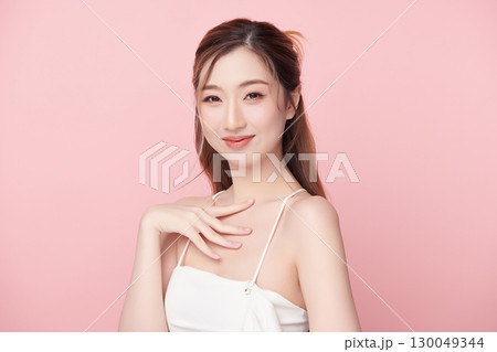 A beautiful young Asian woman with clean, fresh skin against a pink background. Skincare, facial treatment, cosmetology, beauty, and spa. An elegant portrait of an Asian woman. 130049344
