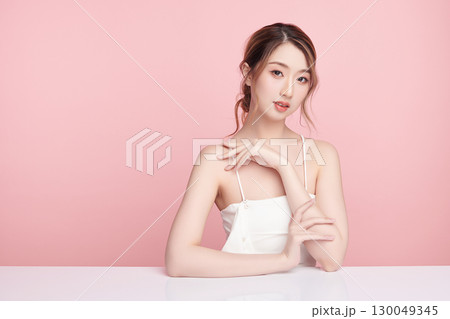 A beautiful young Asian woman with clean, fresh skin against a pink background. Skincare, facial treatment, cosmetology, beauty, and spa. An elegant portrait of an Asian woman. 130049345