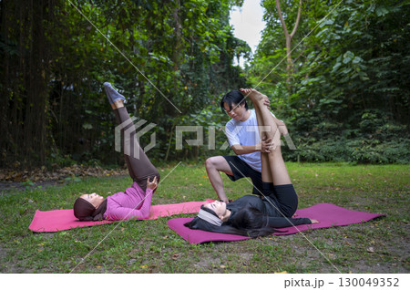 Indonesian southeast asian women in a sporty outfit practice exercise on a mat with a personal trainer man in a public park outdoors. Concept of a Healthy active lifestyle 130049352