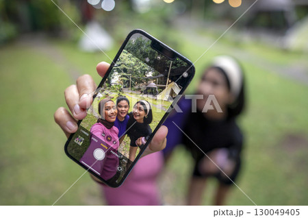 Indonesian southeast asian women in a sporty outfit with a cellphone taking a selfie together after practice exercise in a public park outdoors. Concept of a Healthy active lifestyle 130049405