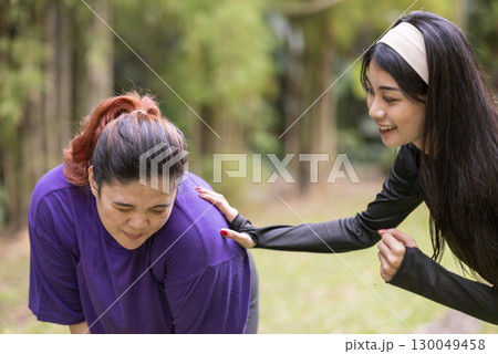Indonesian southeast asian women in a sporty outfit encouraging her friend while running exercise in a public park outdoors. Concept of a Healthy active lifestyle Indonesian southeast asian women in a sporty outfit encouraging her friend while running exercise in a public park outdoors. Concept of a Healthy active lifestyle 130049458
