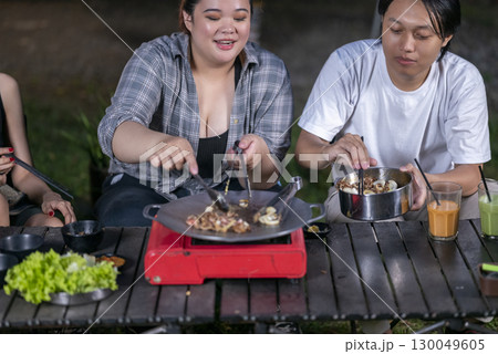 Indonesian southeast asian people with tongs cooking sliced marinated beef bulgogi on a round grill pan with onions. The scene of the lifestyle of enjoying food in a natural setting Indonesian southeast asian people with tongs cooking sliced marinated beef bulgogi on a round grill pan with onions. The scene of the lifestyle of enjoying food in a natural setting 130049605