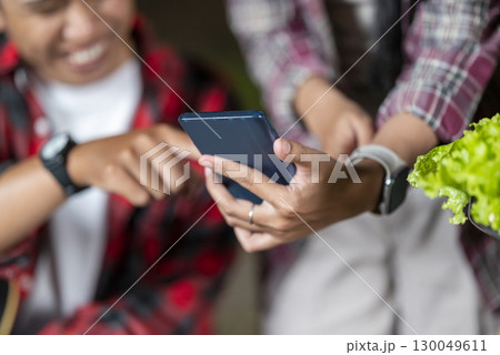 Indonesian southeast asian people enjoying quality time together. Man holds a guitar, and the other women show something on her cellphone. Scene of a lifestyle of enjoying camping in a natural setting 130049611