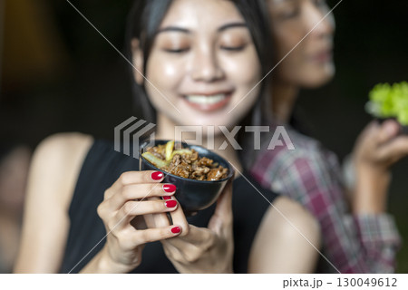 Indonesian southeast asian women holding a plate of vibrant and fresh green lettuce and a bowl of delicious Korean barbecue meal. The scene of the lifestyle of enjoying food in a natural setting 130049612