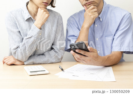 スマホを見て悩む夫婦　白バック 130050209