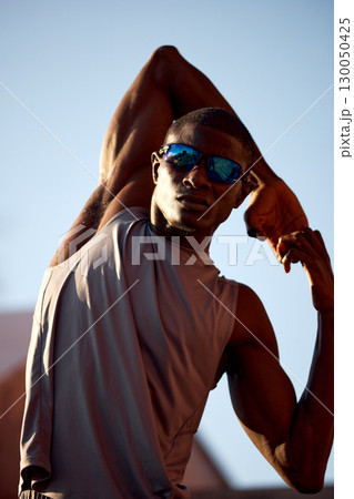 Man stretching his arm outdoors wearing athletic clothing and sunglasses Man stretching his arm outdoors wearing athletic clothing and sunglasses 130050425