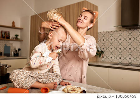 Mother styling daughter's hair in the kitchen during a playful breakfast moment Mother styling daughter's hair in the kitchen during a playful breakfast moment 130050459