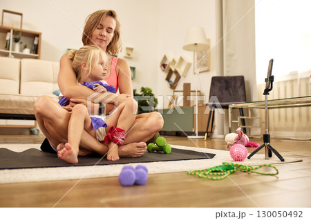 Mother and daughter bonding while exercising in a cozy home setting 130050492