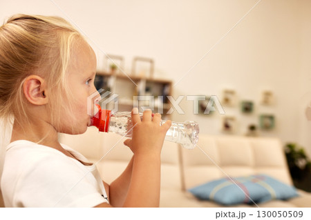 Young girl drinking water from a bottle at home in a relaxed setting 130050509