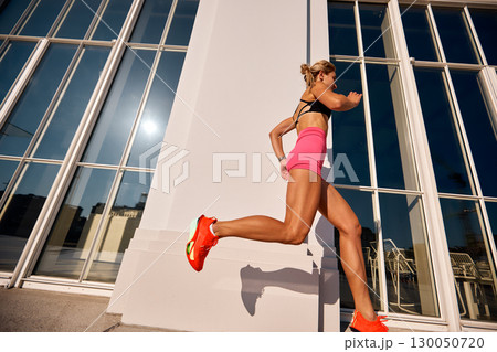 Athletic woman running outdoors near a modern building with glass windows Athletic woman running outdoors near a modern building with glass windows 130050720