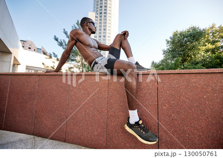 Athletic man resting outdoors on a brick wall in an urban city setting 130050761