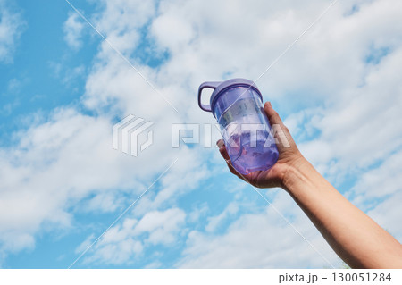 Female hand holding bottle of water against blue sky, bottom-up view 130051284