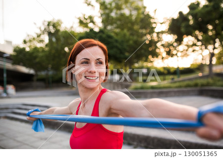 Young woman doing exercise outdoors in city with elastic bands. Young woman doing exercise outdoors in city with elastic bands. 130051365