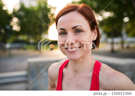 Front view of young woman standing outdoors in city, resting after exercise. Front view of young woman standing outdoors in city, resting after exercise. 130051366