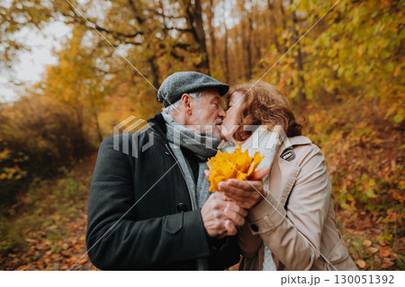 Senior man and woman enjoying a walk in fall, holding fallen leaves. 130051392