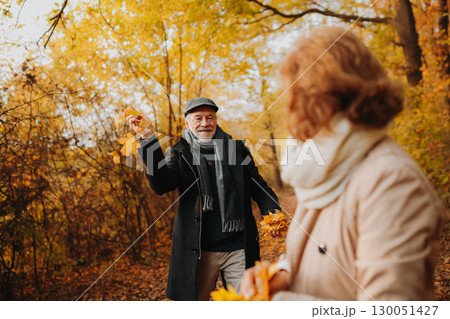 Senior man and woman enjoying a walk in fall, throwing fallen leaves. Senior man and woman enjoying a walk in fall, throwing fallen leaves. 130051427