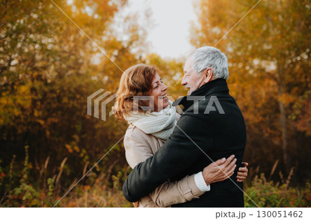 Romantic walk through fall forest by senior couple. 130051462