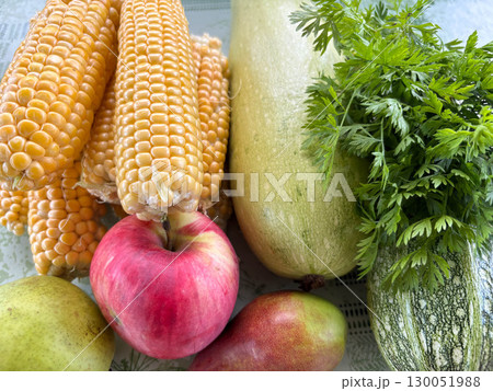 Close-up of fresh vegetables stacked on a table. Corn, zucchini and apples together. A bunch of fresh parsley. Close-up of fresh vegetables stacked on a table. Corn, zucchini and apples together. A bunch of fresh parsley. 130051988