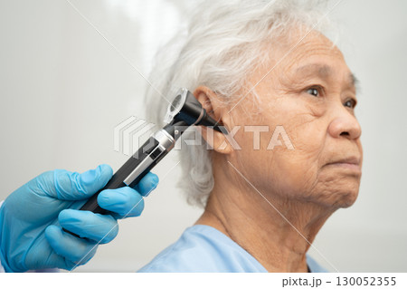 Otolaryngologist or ENT physician doctor examining senior patient ear with otoscope, hearing loss problem. 130052355