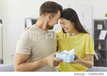 Happy woman receiving surprise gift from beloved man and hugs him warmly 130052865