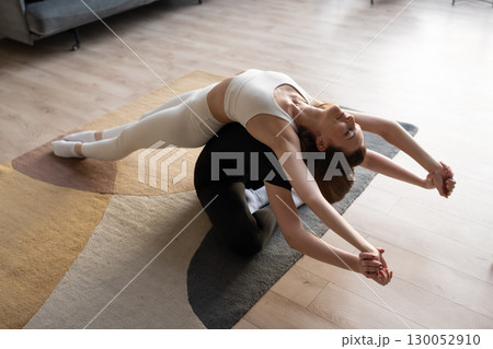 Two women supporting each other in yoga partner pose with balance and mindful stretching indoors. Two women supporting each other in yoga partner pose with balance and mindful stretching indoors. 130052910