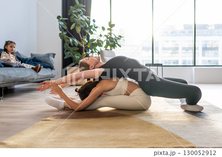 Two women doing acro yoga stretch at home, partner balance exercise with strength, flexibility and posture focus. Two women doing acro yoga stretch at home, partner balance exercise with strength, flexibility and posture focus. 130052912