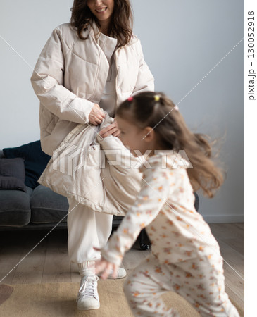 Girl runs across room as mother follows with coat at home 130052918