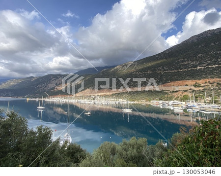 Scenic view of marina with sailboats against mountains and clouds reflecting on water 130053046