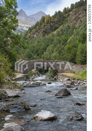 Scenic view of Pyrenees stone bridge over Gavarnie stream at dawn, surrounded by lush greenery and 130053556