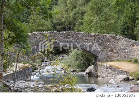 Scenic view of Pyrenees stone bridge over Gavarnie stream at dawn, surrounded by lush greenery and 130053678