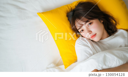 黄色い枕に寄り添って横になる女性 130054128