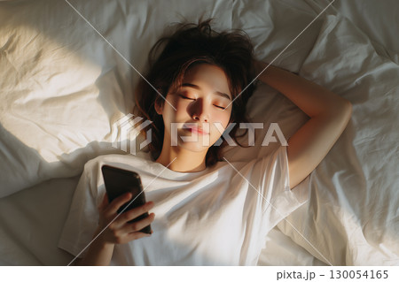 ベッドでスマートフォンを見ながら横になる女性 130054165