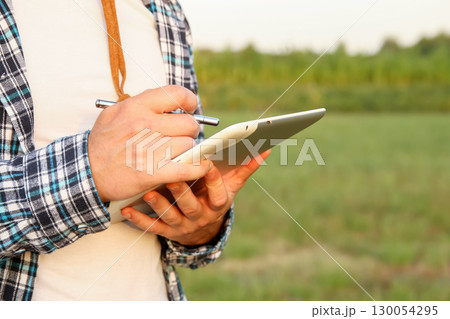a farmer using a tablet in a farm field. farmer with tablet agriculture AI. smart farming technology data science. precision agriculture crop management 130054295