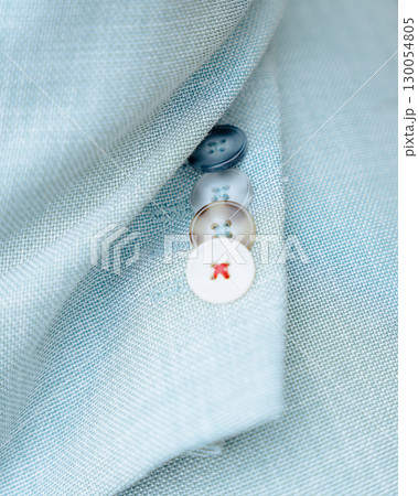 Macro shot of a light blue textured jacket sleeve with four decorative buttons. One of the buttons has red stitching detail, creating a stylish and unique fashion accent. Perfect for illustrating 130054805