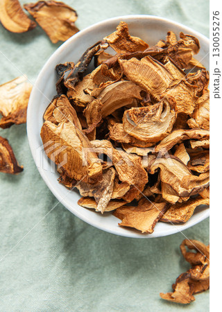 Dried mushrooms in a bowl resting on a green cloth 130055276