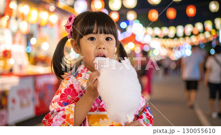 日本の夜の夏祭りの縁日で綿菓子を美味しそうに食べる浴衣姿の幼くて可愛い女の子 130055610