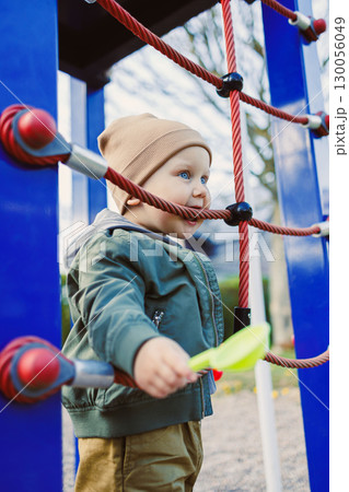 A joyful toddler explores an outdoor climbing structure, enjoying autumns colors and crisp air in a safe environment with their loving family, fostering growth and creativity together 130056049
