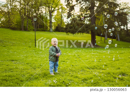 Little 2 year old boy running on green grass with soap bubbles. Toddler boy enjoying a walk in nature. Child having fun in city park. Little 2 year old boy running on green grass with soap bubbles. Toddler boy enjoying a walk in nature. Child having fun in city park. 130056063