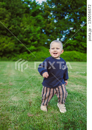 Toddler laughing and enjoying warm sunny day. Happy 2 year old boy in t-shirt and shorts running on green grass and laughing outdoors. Child playing on public playground on sunny summer day. Toddler laughing and enjoying warm sunny day. Happy 2 year old boy in t-shirt and shorts running on green grass and laughing outdoors. Child playing on public playground on sunny summer day. 130056072