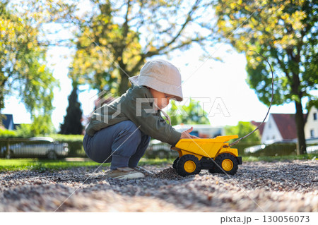Toddler boy playing on the playground outside with his plastic car. Cute 2 year old boy playing with a car in the yard. Child walking outdoors. Toddler boy playing on the playground outside with his plastic car. Cute 2 year old boy playing with a car in the yard. Child walking outdoors. 130056073